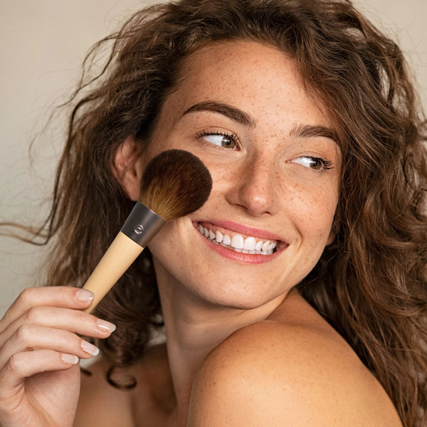 Powder makeup brush with rounded brown bristles and light wood handle
