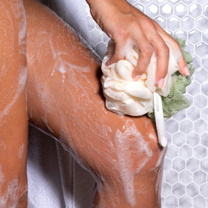 Hand using a white-and-green bath loofah pouf for gentle skin cleansing