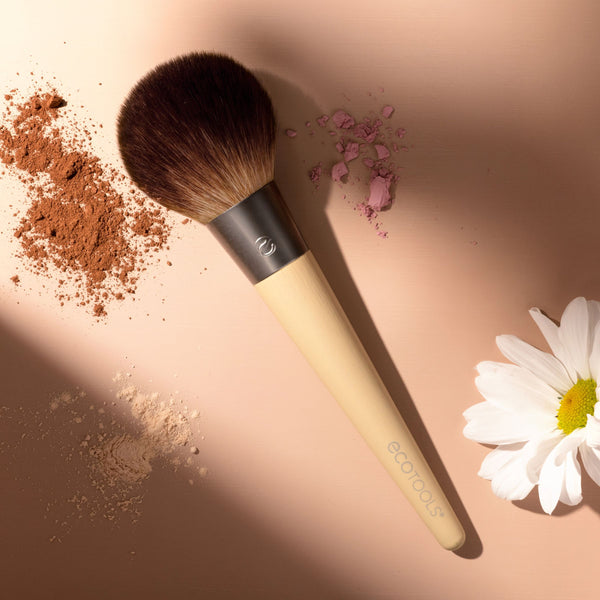 Powder makeup brush with dense brown brush head on pale wood handle