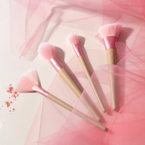 Four makeup brushes with soft pink bristles and beige handles, brushed in a fan arrangement.