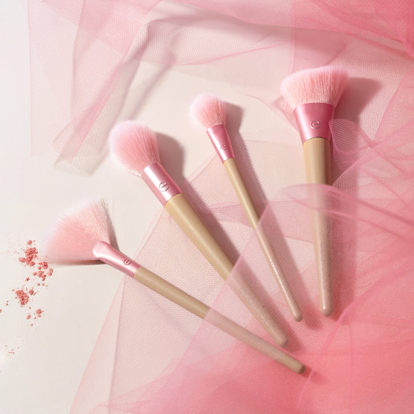 Four makeup brushes with soft pink bristles and beige handles, brushed in a fan arrangement.