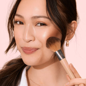 Makeup brush with beige handle and silver ferrule, rounded brown bristles blending makeup