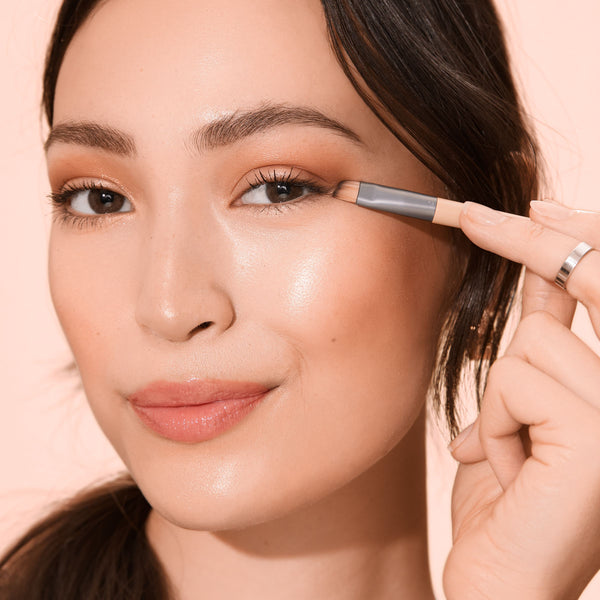 Woman applying eye makeup with a tapered brown-bristle makeup brush near eyebrow