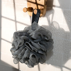 Charcoal bath sponge pouf made of dark gray mesh with a hanging loop