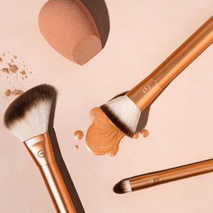 Two gold makeup brushes with powder on bristles plus teardrop blending sponge.