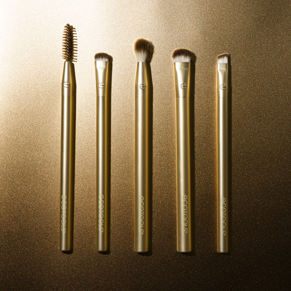 Five gold eye makeup brushes with dark brown bristles, arranged upright.