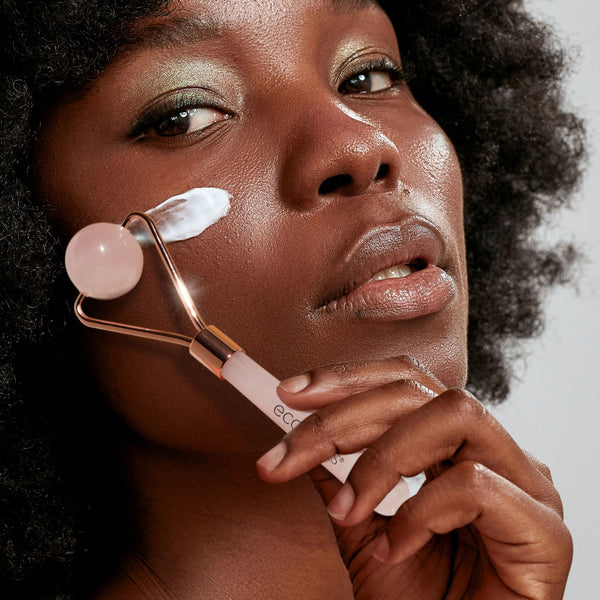 Facial roller being used on cheek: rose quartz round stone head with rose-gold frame