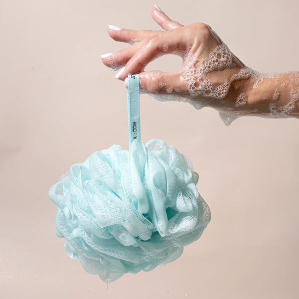 Light blue mesh cleansing pouf hanging from a wrist with suds