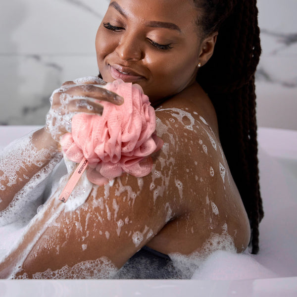 Pink EcoPouf in hand with bubble lather visible on the skin