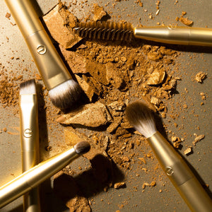 Close-up of gold eye brushes with dark brown bristles, including spoolie head.