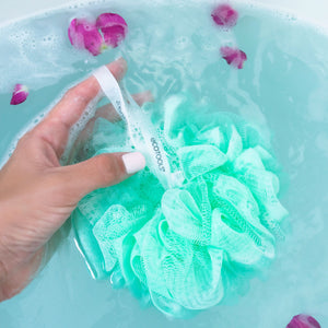 Green and white exfoliating bath sponge, held in hand with hanging loop, mesh texture