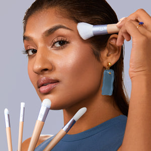 Skincare brush with short white bristles used for under-eye blending near the face.