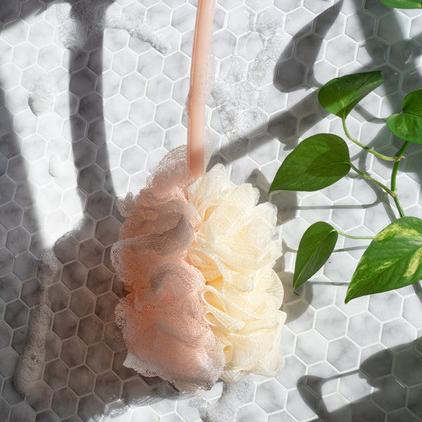 Cream loofah bath brush head with scrubbing net, on long light pink handle