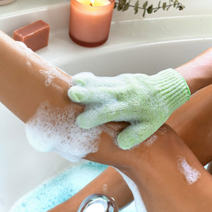 Green exfoliating shower glove on hand, lathered scrub surface
