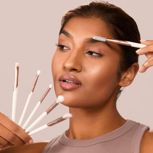 Woman applying eye makeup while holding rose-gold eye brushes with white bristles