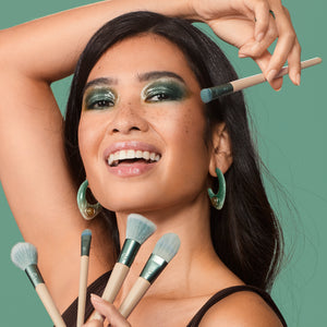 Teal-handled face makeup brush being used on a person applying makeup