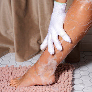 White exfoliating bath glove with green cuff on foot, showing textured scrubbing fabric.