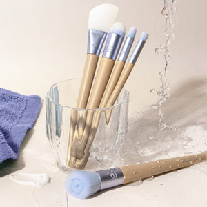 Skincare brushes with blue handles and white bristles in a cup with water splash.