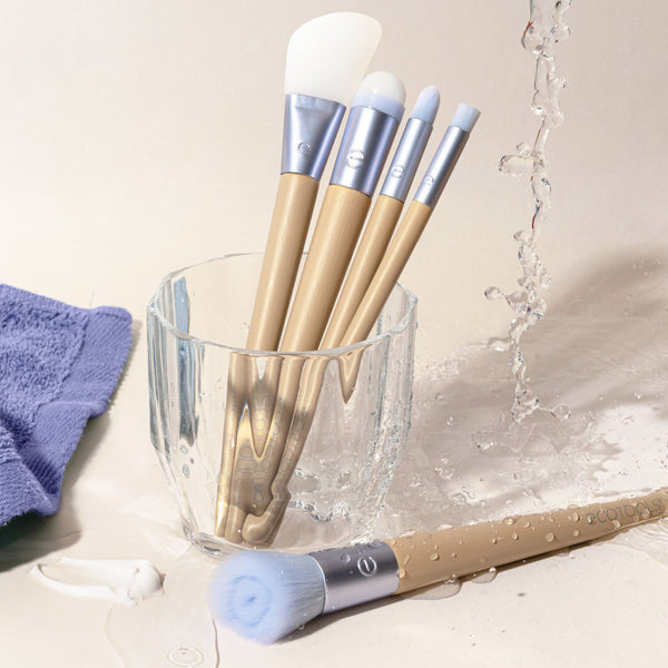 Skincare brushes with blue handles and white bristles in a cup with water splash.