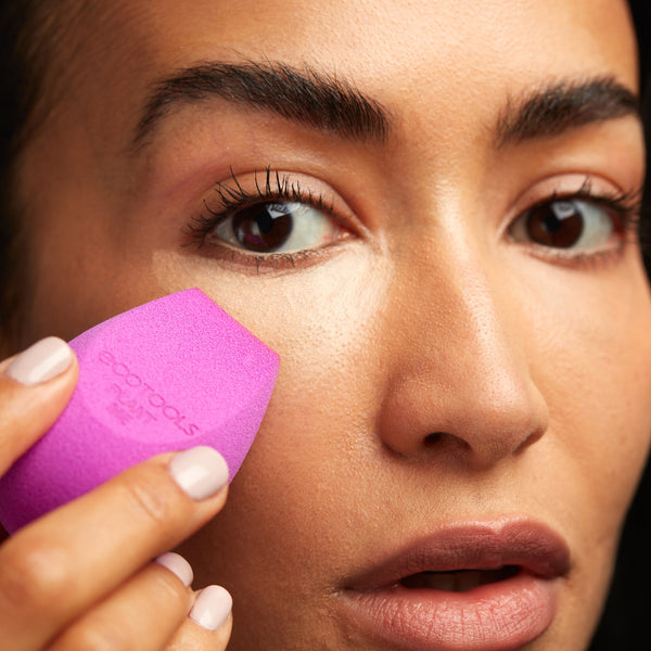 Purple teardrop makeup sponge held to apply foundation for smooth blended coverage