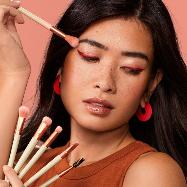 Person applying eye makeup with peach blending brush and visible spoolie from brush kit